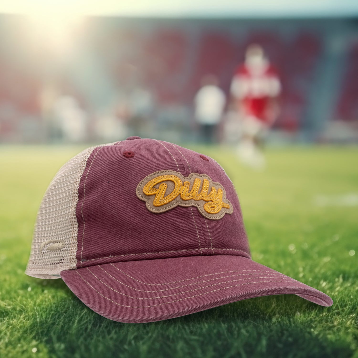 Maroon cap with 'Dilly' logo on grass, blurred sports background