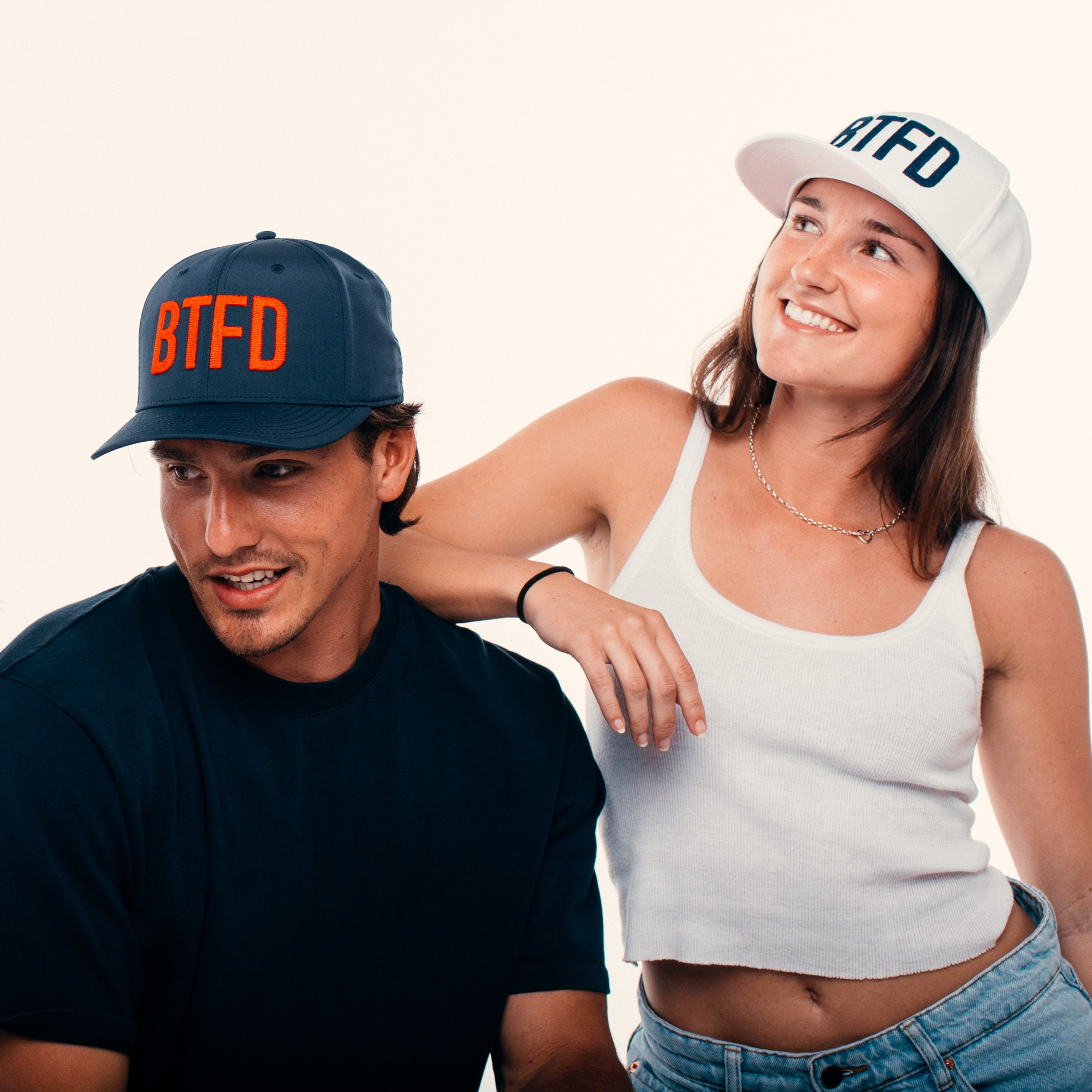 Two people wearing caps with 'BTFD' text, one navy and one white, on a plain background.